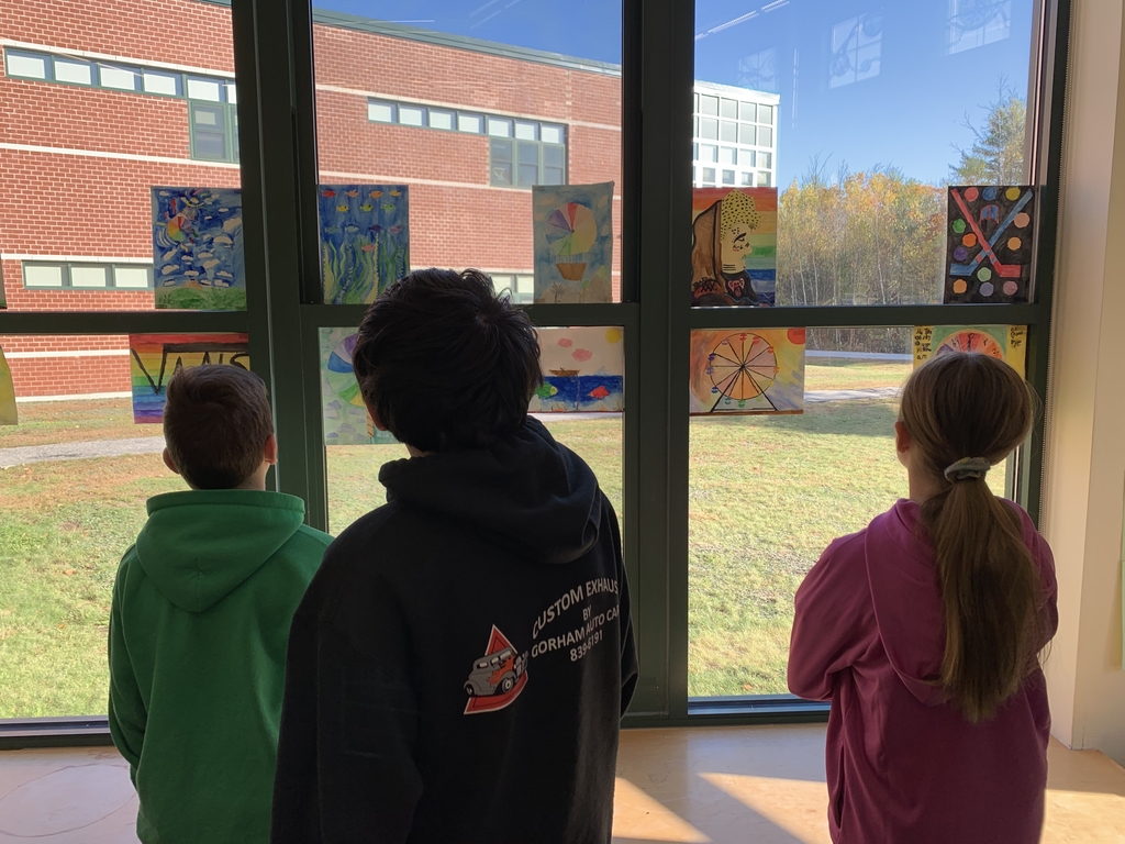 Students viewing watercolor artwork hung on the windows of the MMS library.